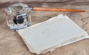 Mustekynä ja -pullo sekä vanhoja kirjeitä pöydällä.